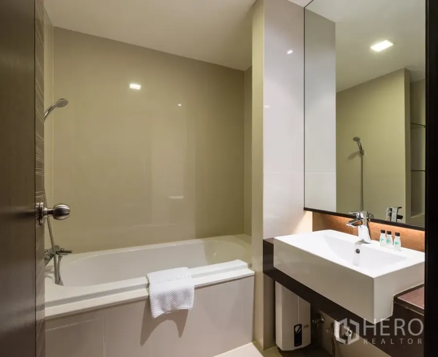 Apartment for rent in Khlong Toei, Bangkok - Modern bathroom with bathtub, wall shower, large mirror and vanity in a Bangkok apartment.