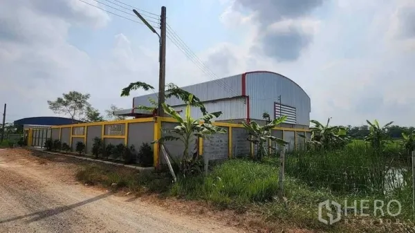 Warehouse for rent in Nong Chok, Bangkok - Corner view of the warehouse compound beside a rural road and canal with greenery.