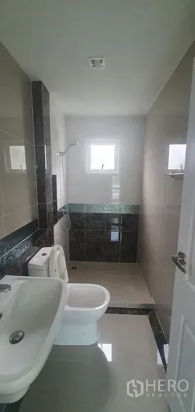 Detached House for rent in Nonthaburi - Bright tiled bathroom with window, shower zone, sink and toilet in a detached house in Pak Kret, Nonthaburi.