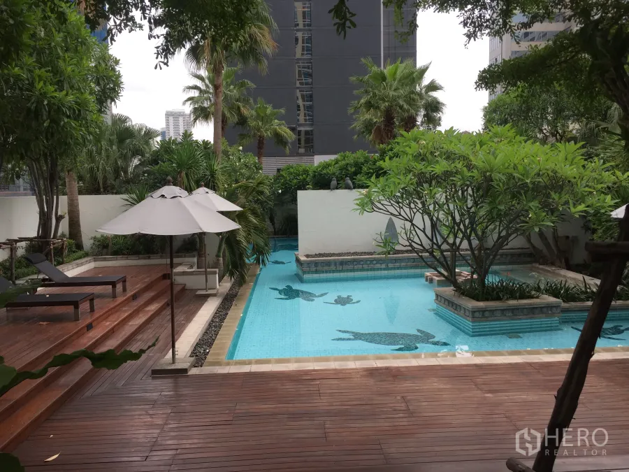 Condominium for rent in Pathum Wan, Bangkok - Resort-style condominium swimming pool with wooden sundeck, sun loungers and lush tropical trees.