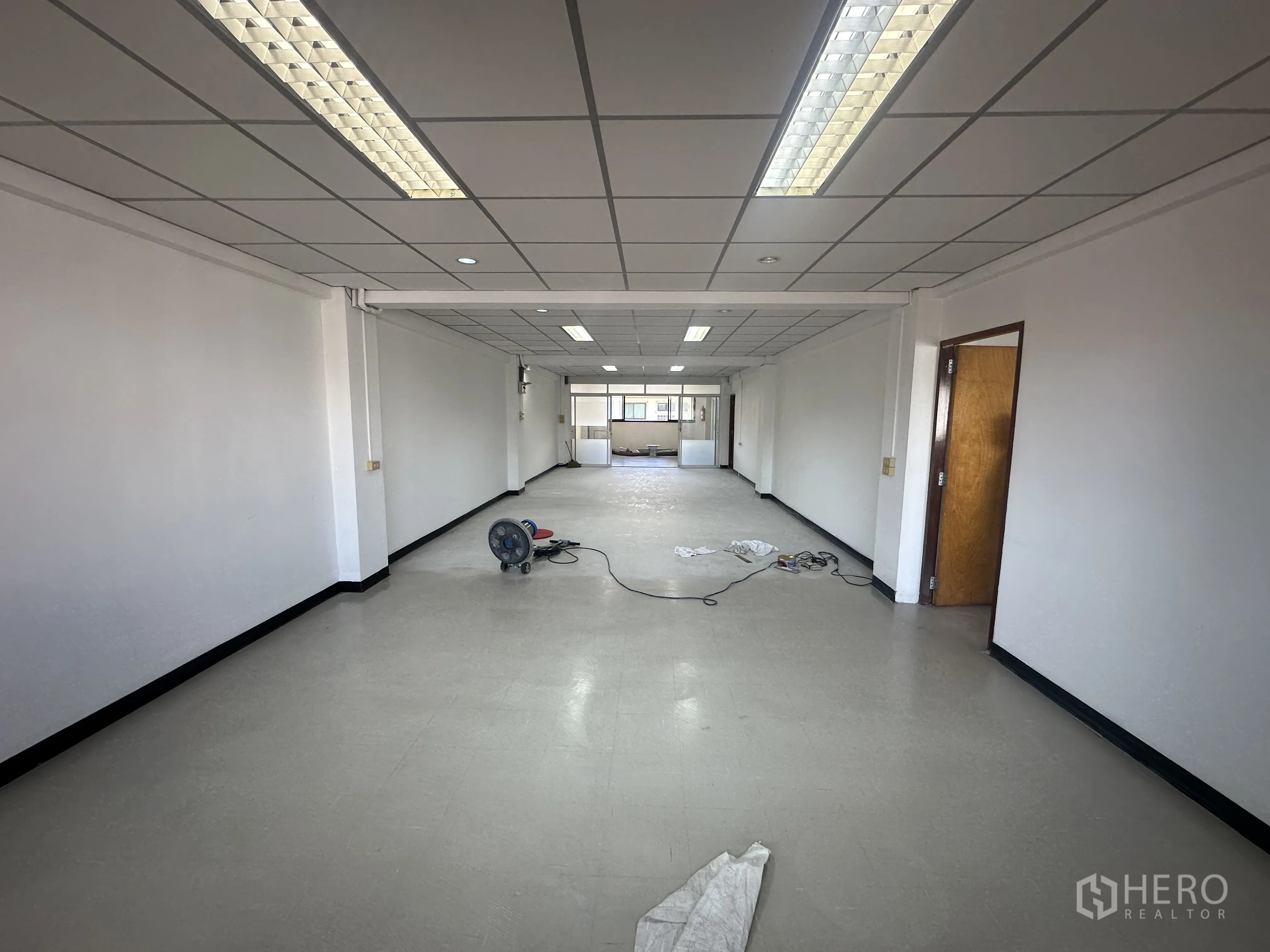ออฟฟิศ for rent in Watthana, Bangkok - สำนักงานแบบโอเพ่นสเปซยาว เพดานแผ่นสำเร็จไฟฟลูออเรสเซนต์ ผนังสีขาวและพื้นไวนิล พร้อมพัดลมและสายไฟบนพื้น
