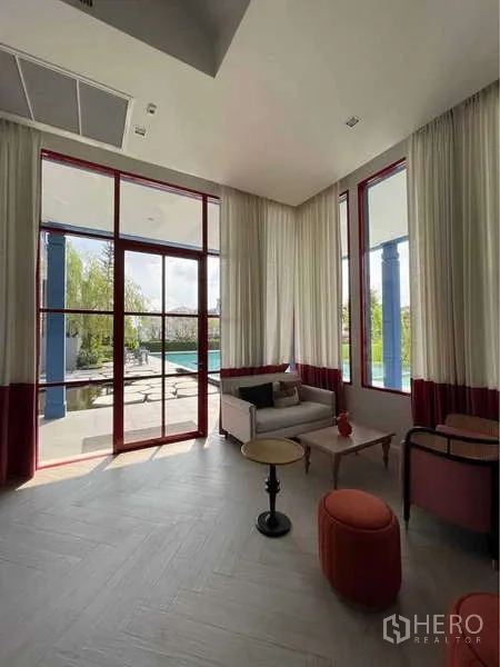 Detached House for rent in Prawet, Bangkok - Clubhouse lounge from another angle with tall drapes and pool view.