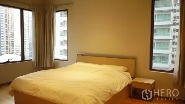Condominium for rent in Khlong Toei, Bangkok - Corner master bedroom with king bed, bedside table and panoramic windows overlooking the Bangkok skyline.