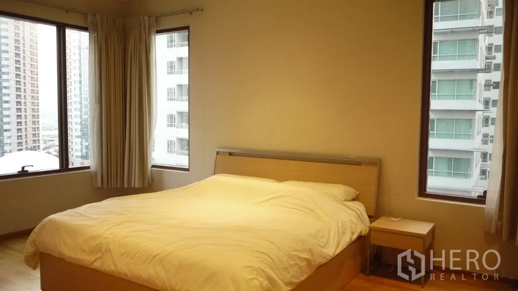 Condominium for rent in Khlong Toei, Bangkok - Corner master bedroom with king bed, bedside table and panoramic windows overlooking the Bangkok skyline.