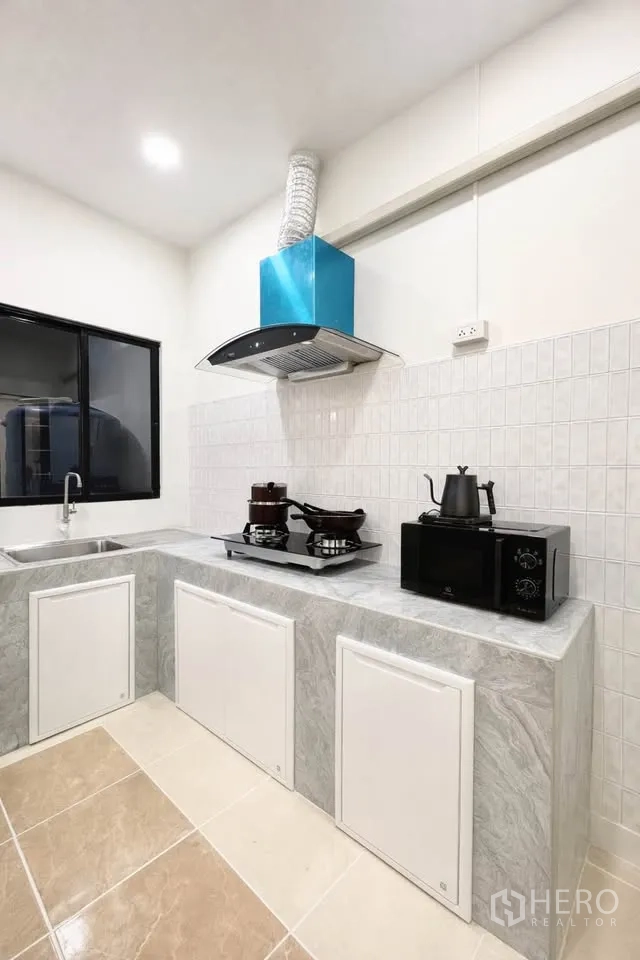 Detached House for rent in Huai Khwang, Bangkok - Modern kitchen with marble-look counters, hob, hood, sink and microwave.