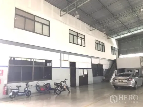 Factory for rent in Bang Bua Thong, Nonthaburi - Bright factory hall with mezzanine offices, concrete floor and parked vehicles.