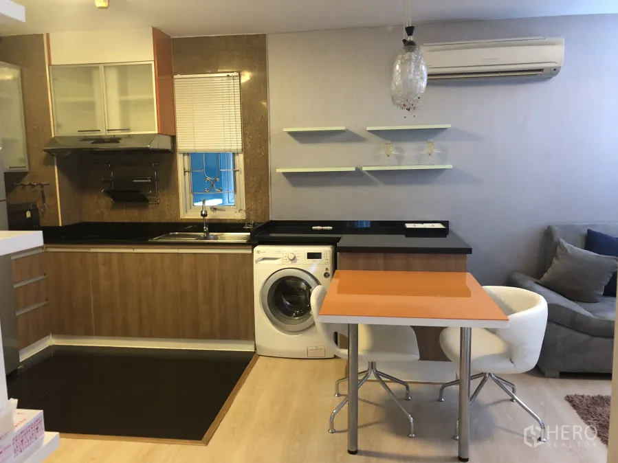 Condominium for rent or sale in Khlong Toei, Bangkok - Open-plan kitchen with wooden cabinets, black countertops, sink, and a washing machine beside a breakfast bar.