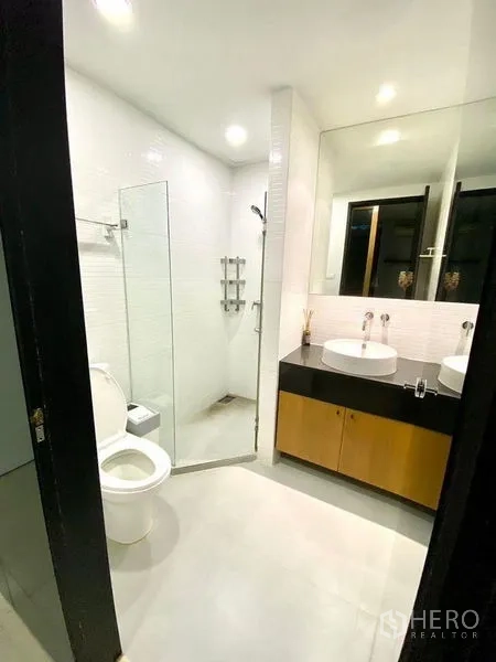 Condominium for rent in Chatuchak, Bangkok - Bathroom with glass-enclosed shower and double vanity beneath a wide mirror.