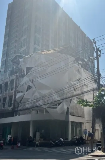 Shophouse for rent in Watthana, Bangkok - Corner shophouse exterior with large glass frontage and white facade covering on a sunny street.