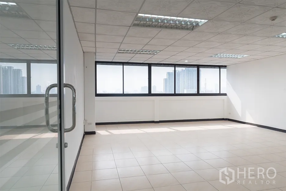 Office Space for rent in Din Daeng, Bangkok - Bright empty office with tiled floors, drop‑ceiling lights, and wide windows offering Bangkok skyline views, seen through a glass door.