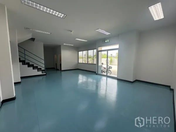 Factory for rent in Bang Phli, Samut Prakan - Bright ground-floor office or showroom with blue epoxy floor, staircase and fluorescent lighting.