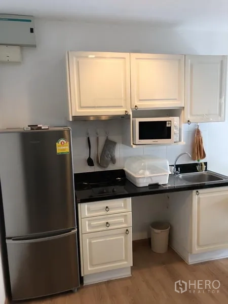 Condominium for rent in Pathum Wan, Bangkok - Compact kitchenette with white cabinets, black countertop, sink, microwave and stainless refrigerator.