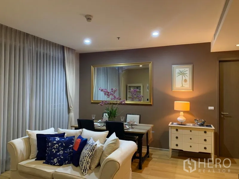 Condominium for rent in Watthana, Bangkok - Warm living and dining area with cream sofa, set dining table, large wall mirror and soft ambient lighting.