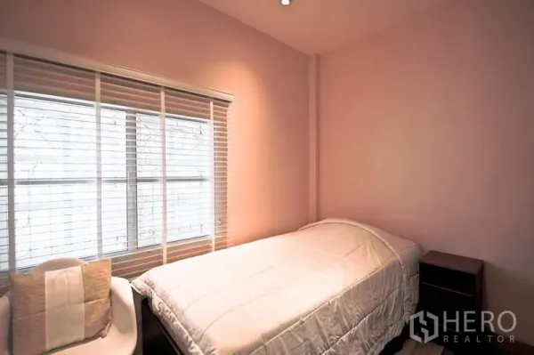Detached House for rent in Bang Kapi, Bangkok - Cozy single bedroom with pink walls, window blinds, white armchair, and bedside table.
