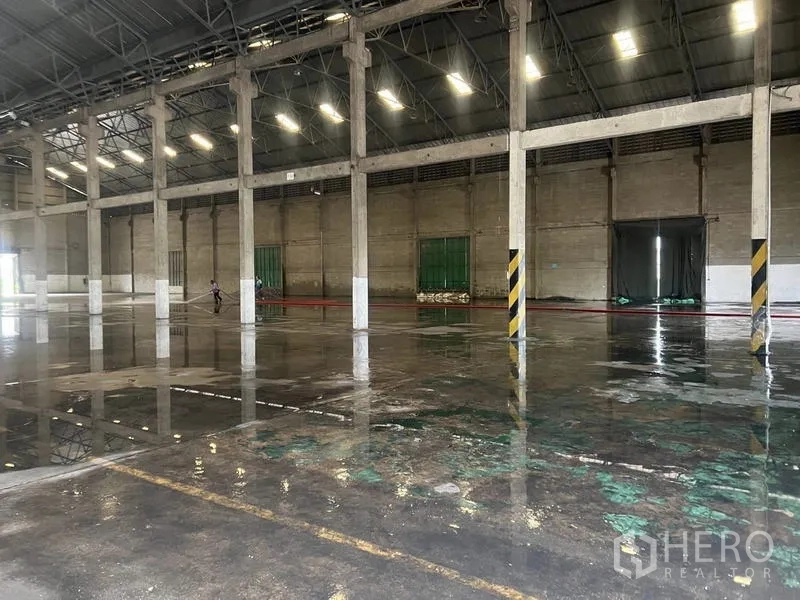 Warehouse for rent in Mueang Pathum Thani, Pathum Thani - Wet concrete floor after washdown reflecting roof lights and structural columns.