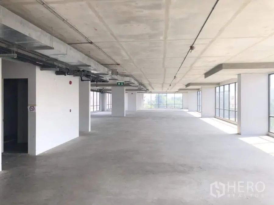 Office Space for rent in Suan Luang, Bangkok - Open-plan office floor with exposed ceiling ducts, white columns, and full-height windows filling the space with natural light.