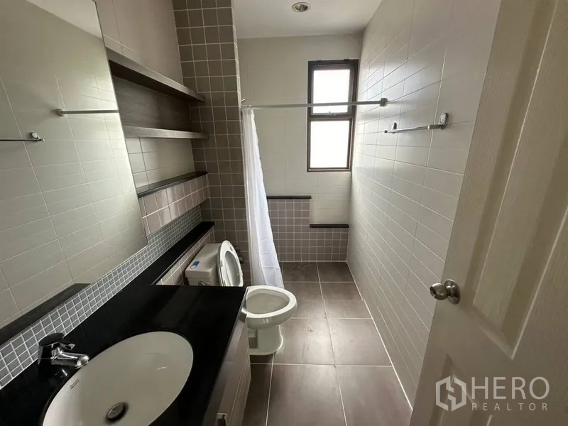 Townhouse for rent or sale in Phra Khanong, Bangkok - Long bathroom with window, black-top vanity, and shower area.