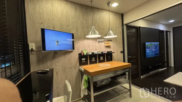 Condominium for rent or sale in Khlong Toei, Bangkok - Dining nook with wall-mounted TV, pendant lights and a wooden island workstation.