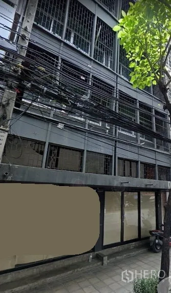 店屋 出租在Phra Khanong, Bangkok - 帕卡农多层商铺外立面，金属护栏与大面积玻璃门面，路旁树木与电缆，临近Bang Chak BTS。