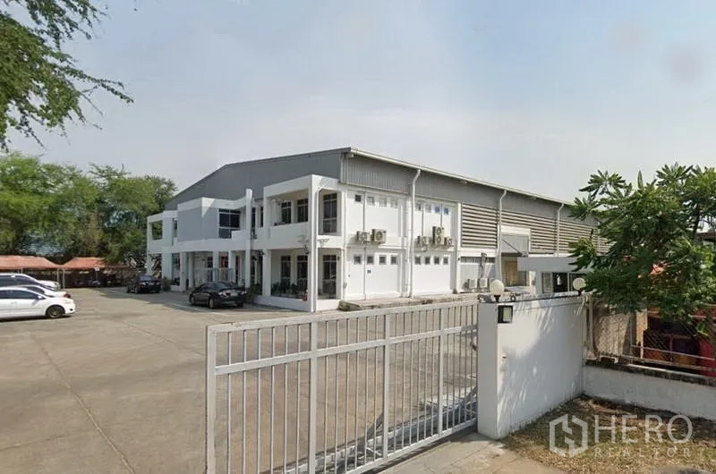 Factory for rent in Mueang Samut Prakan, Samut Prakan - Gated entrance to the industrial property with parking area and a two‑storey office linked to the warehouse.