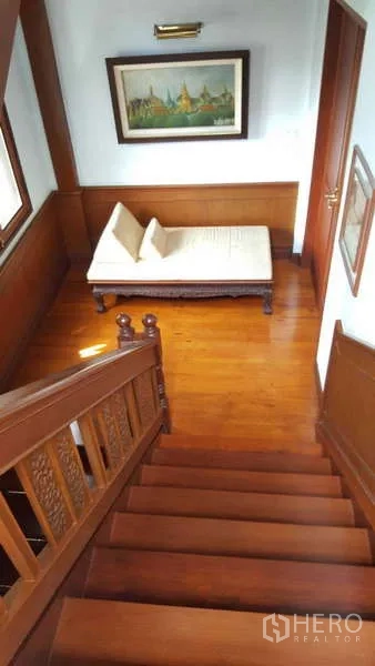 Townhouse for rent in Khlong Toei, Bangkok - Polished wooden staircase leading to landing with daybed and artwork.