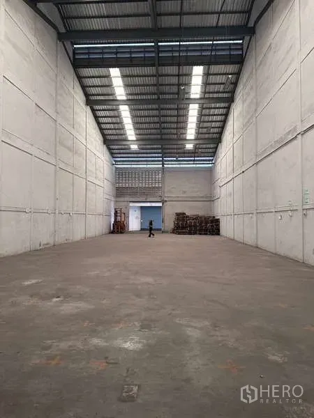 Warehouse for rent in Mueang Samut Prakan, Samut Prakan - Empty high-clearance warehouse hall with concrete floor and skylights.