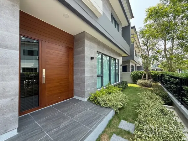 Detached House for rent in Bang Phli, Samut Prakan - Wide wooden front door with tiled porch beside a landscaped front garden of shrubs and lawn.