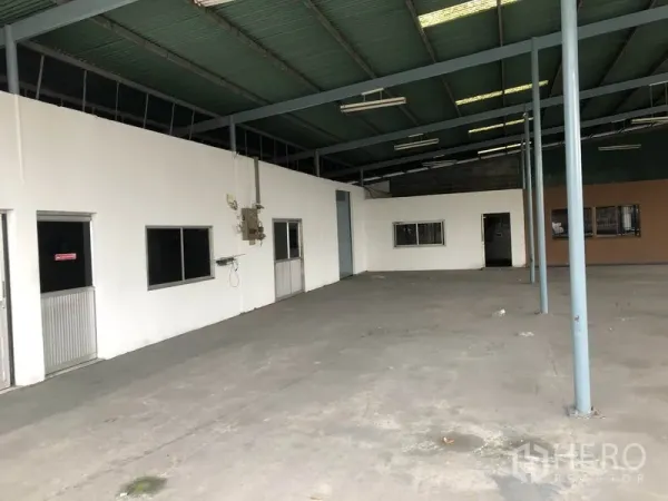 Warehouse for rent in Bang Phli, Samut Prakan - Concrete-floored warehouse facing internal office rooms, service doors, and utility panel.