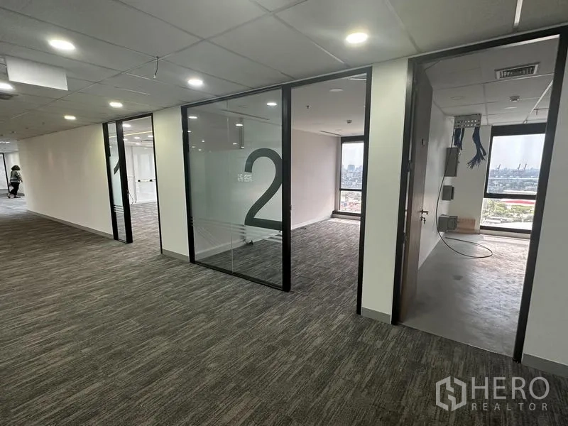 Office Space for rent in Khlong Toei, Bangkok - Corridor with numbered glass offices and a server room under installation, city view beyond.