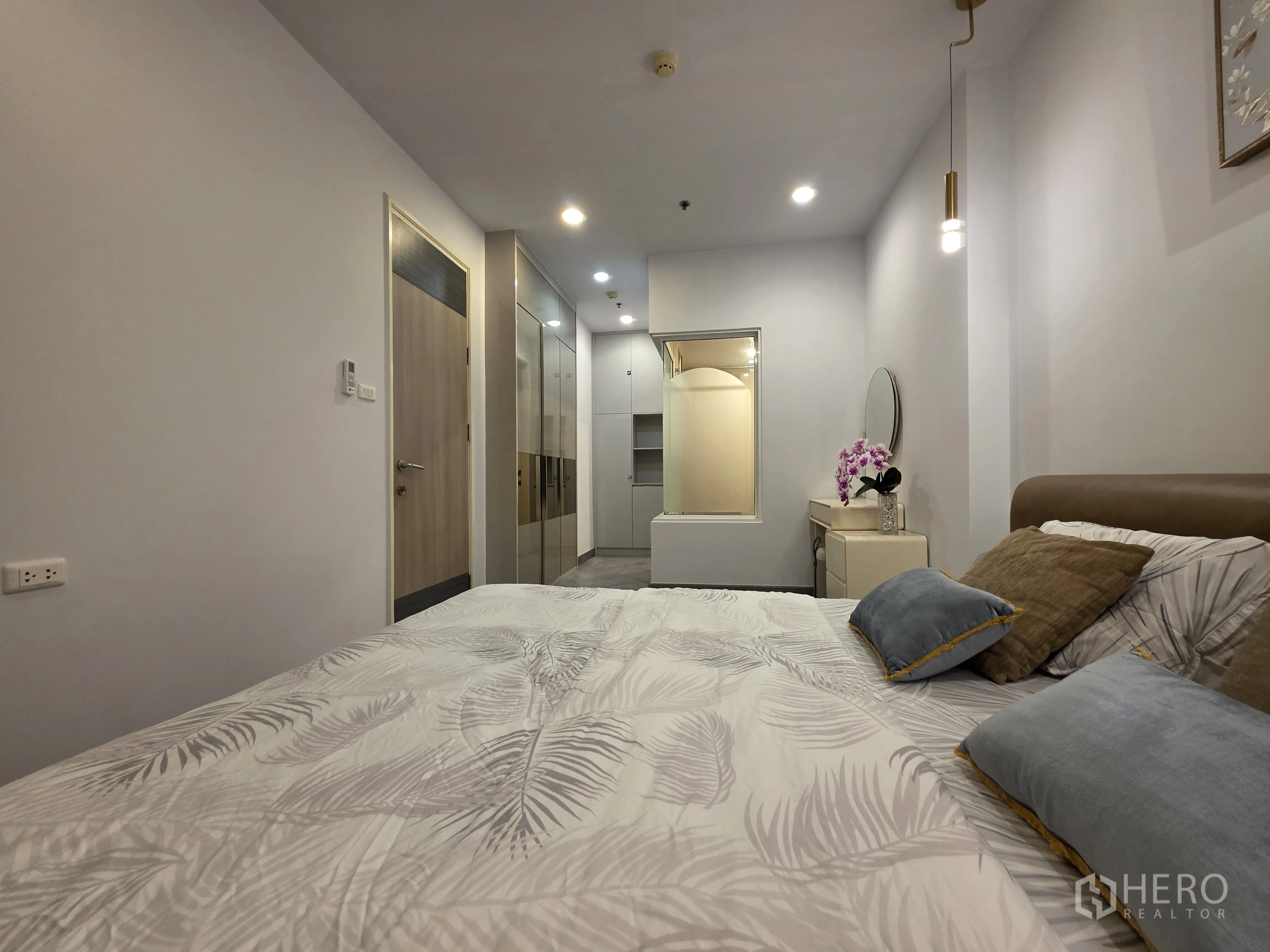 Condominium for rent in Bang Kapi, Bangkok - Bedroom view toward built-in wardrobes and entry door with soft lighting.