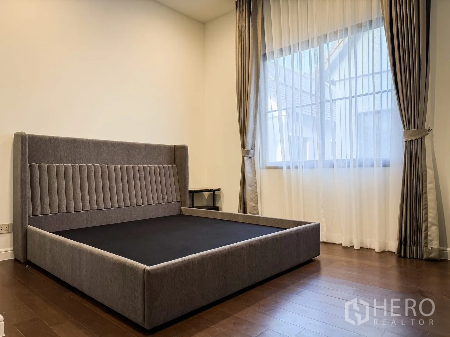 Detached House for rent in Bang Khen, Bangkok - Bedroom with upholstered platform bed, wood flooring and full-length curtains.