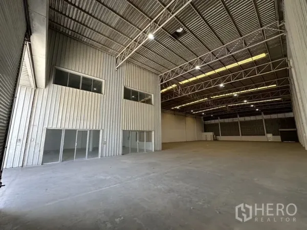 Factory for rent in Khlong Luang, Pathum Thani - Interior view showing two‑storey office block with glass doors beneath a high clear-span ceiling.