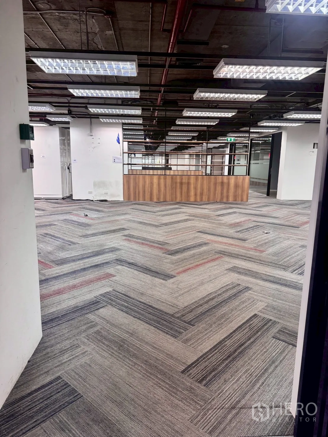 Office Space for rent in Watthana, Bangkok - Open-plan office corridor with herringbone carpet and suspended fluorescent lights leading to a wood reception counter.
