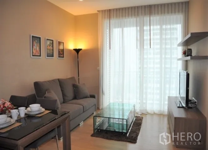 Condominium for rent or sale in Watthana, Bangkok - Bright living and dining area with sofa, glass coffee table, and balcony.
