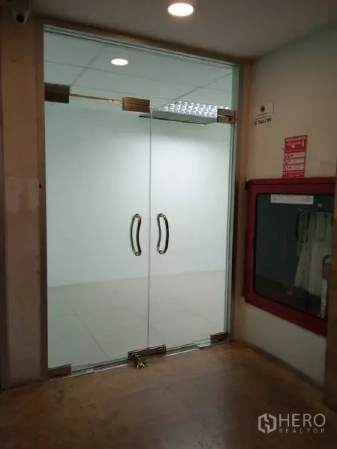 Office Space for rent in Huai Khwang, Bangkok - Glass double-door entrance to the office from the corridor with a fire safety cabinet nearby.