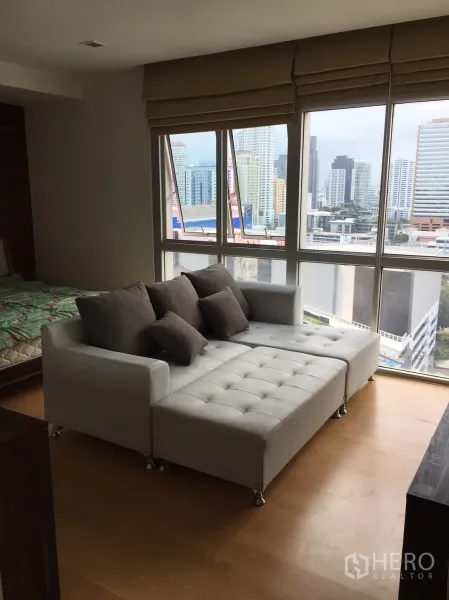 Condominium for rent or sale in Khlong Toei, Bangkok - Sitting area by large windows with a chaise sofa and Bangkok city skyline views.