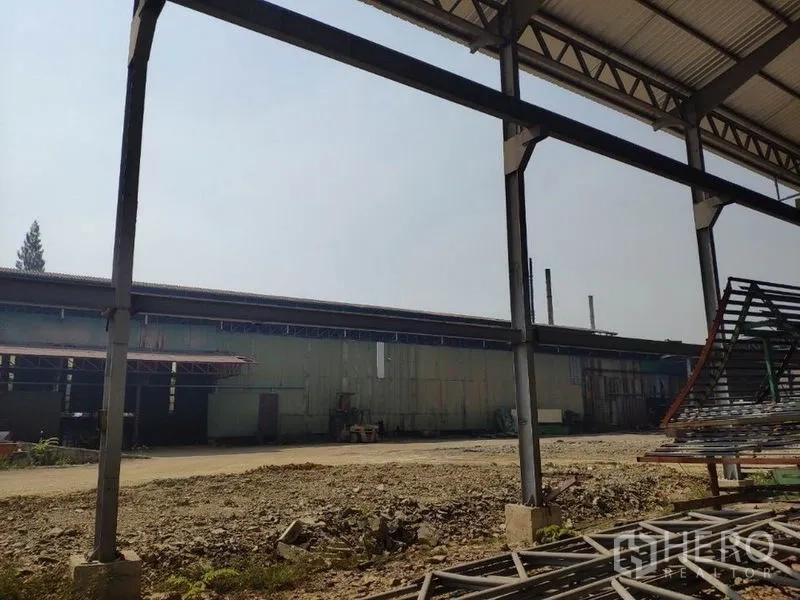 Factory for rent in Samut Sakhon - Covered work bay with steel columns and yard facing an adjacent industrial building in Bang Krachao.