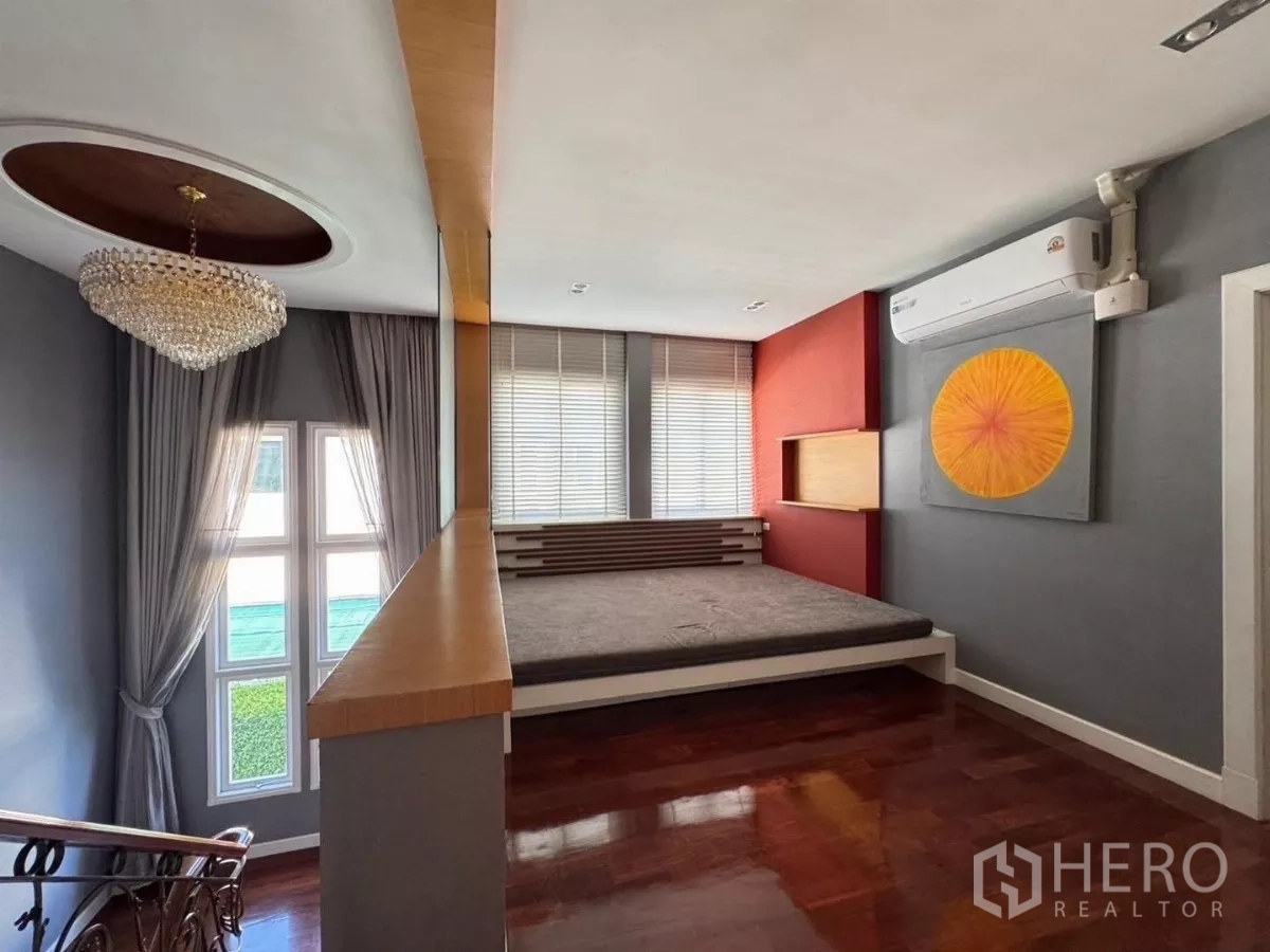 Detached House for rent or sale in Prawet, Bangkok - Upstairs lounge or bedroom with chandelier, platform bed and polished wood floors.