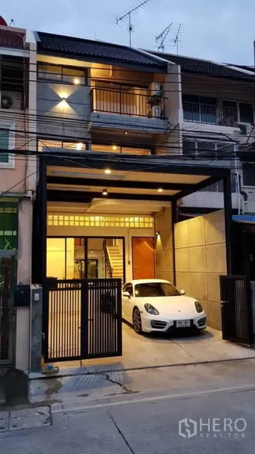 联排别墅 出租在Khlong Toei, Bangkok - 黄昏时的三层联排别墅外观，带电动门车库和一辆白色轿车。