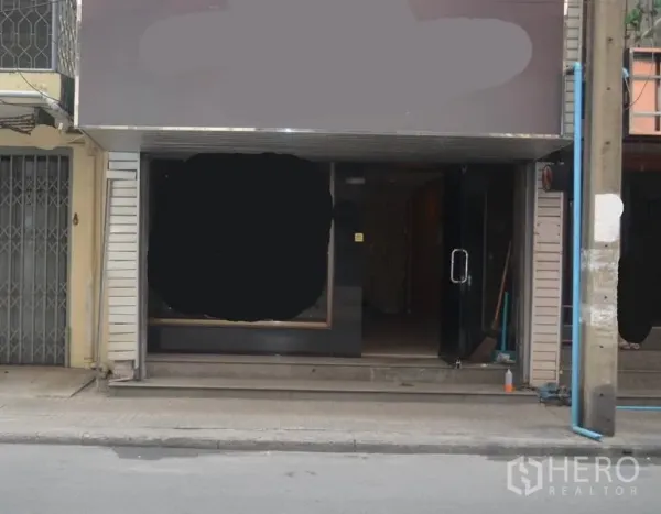 Shophouse for rent in Khlong Toei, Bangkok - Street‑level storefront of a shophouse with large display window and glass door entrance beside a sidewalk and utility pole.