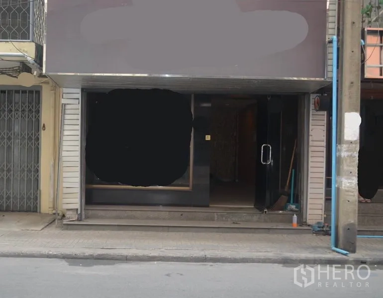Shophouse for rent in Khlong Toei, Bangkok - Street‑level storefront of a shophouse with large display window and glass door entrance beside a sidewalk and utility pole.