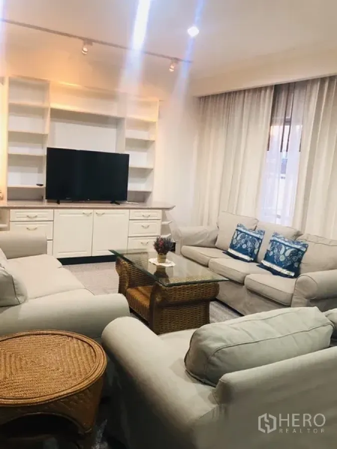 Condominium for rent in Watthana, Bangkok - Spacious living room with white sofas, built-in shelving and a glass coffee table.