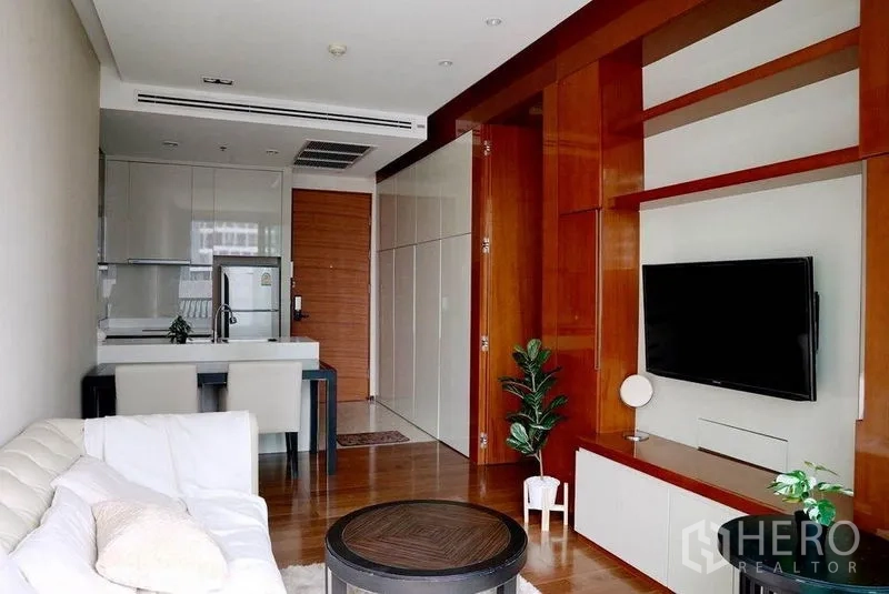 Condominium for rent in Khlong Toei, Bangkok - Open‑plan living and dining area with TV feature wall, kitchen, and wood floors.