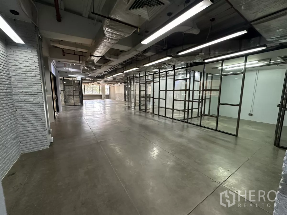 Office Space for rent - Open-plan zone with white brick wall, glass rooms and long LED lights.