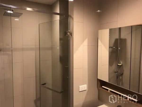 Condominium for rent in Watthana, Bangkok - Modern bathroom with glass-enclosed rain shower and mirrored cabinet.