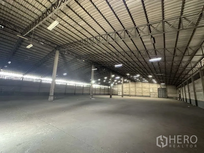 Warehouse for rent in Pak Kret, Nonthaburi - Vast empty warehouse interior with high steel truss roof and industrial lighting.