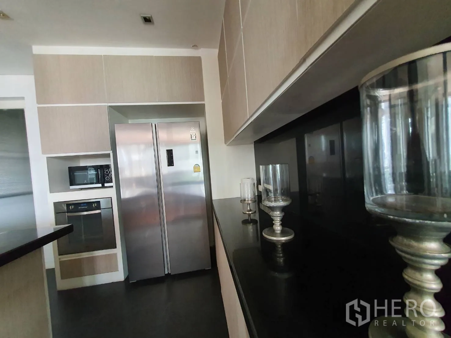 Condominium for rent in Khlong Toei, Bangkok - Kitchen zone with double-door refrigerator, built-in oven and microwave against a black backsplash.