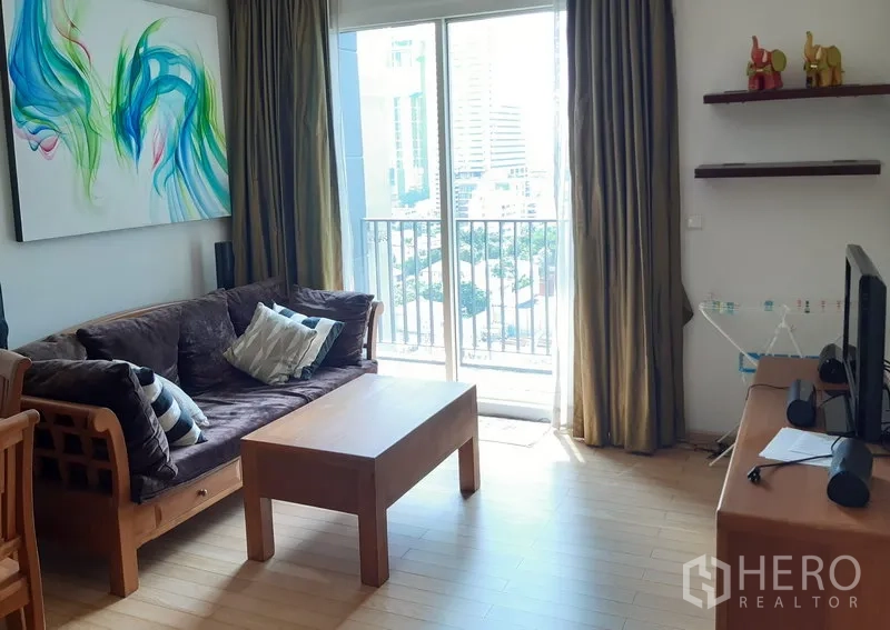 Condominium for rent in Khlong Toei, Bangkok - Bright living room with wooden sofa, coffee table and sliding doors to a balcony with city view.