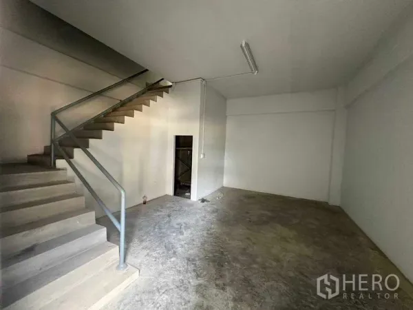 Warehouse for rent in Mueang Samut Sakhon, Samut Sakhon - Ground-floor office or storage room beside an open stair, concrete floor and white walls.