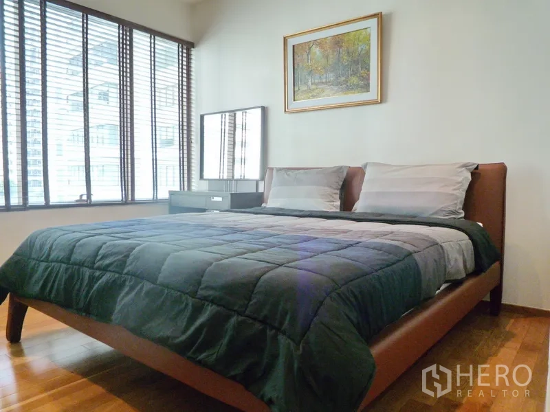 Condominium for rent in Khlong Toei, Bangkok - Cozy second bedroom with large windows, wooden floors and a framed artwork above the bed.